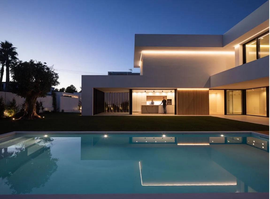 Vista nocturna de la piscina y la vivienda iluminada