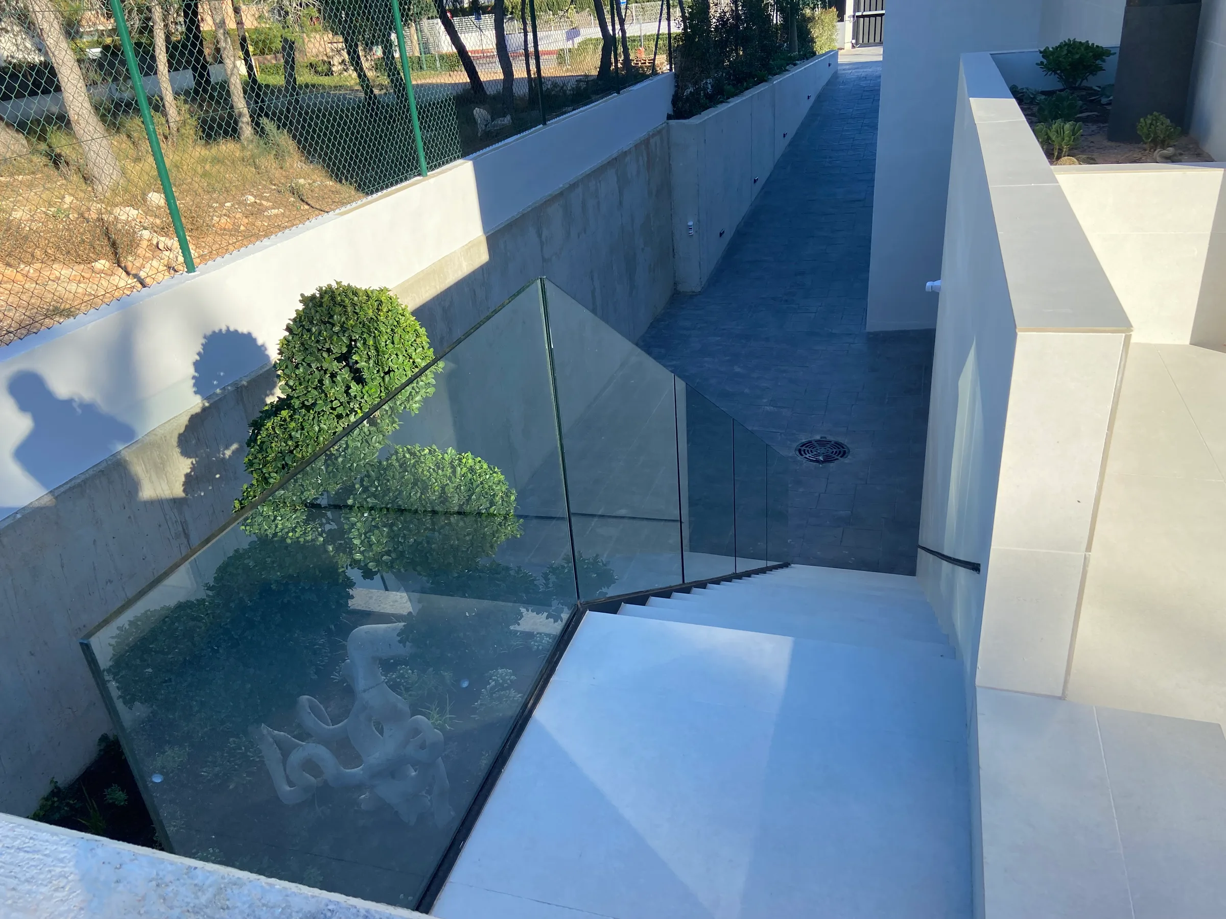 Escalera exterior de bajada al sótano con barandilla de cristal